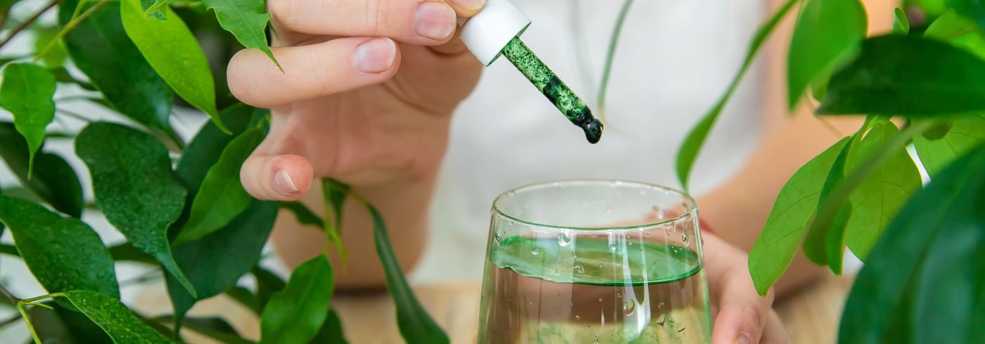 Woman dripping chlorophyll supplement into a glass of water. Selective focus. Drink.